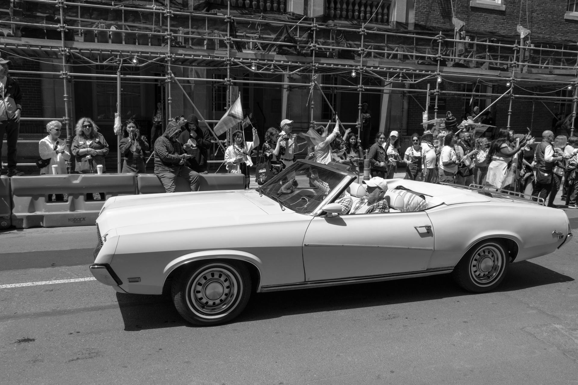 Classic Mercury Cougar convertible drives through a city parade, attracting an excited crowd.