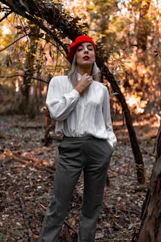 一位优雅女子戴着红色贝雷帽，在风景优美的秋季森林中自信地摆姿势