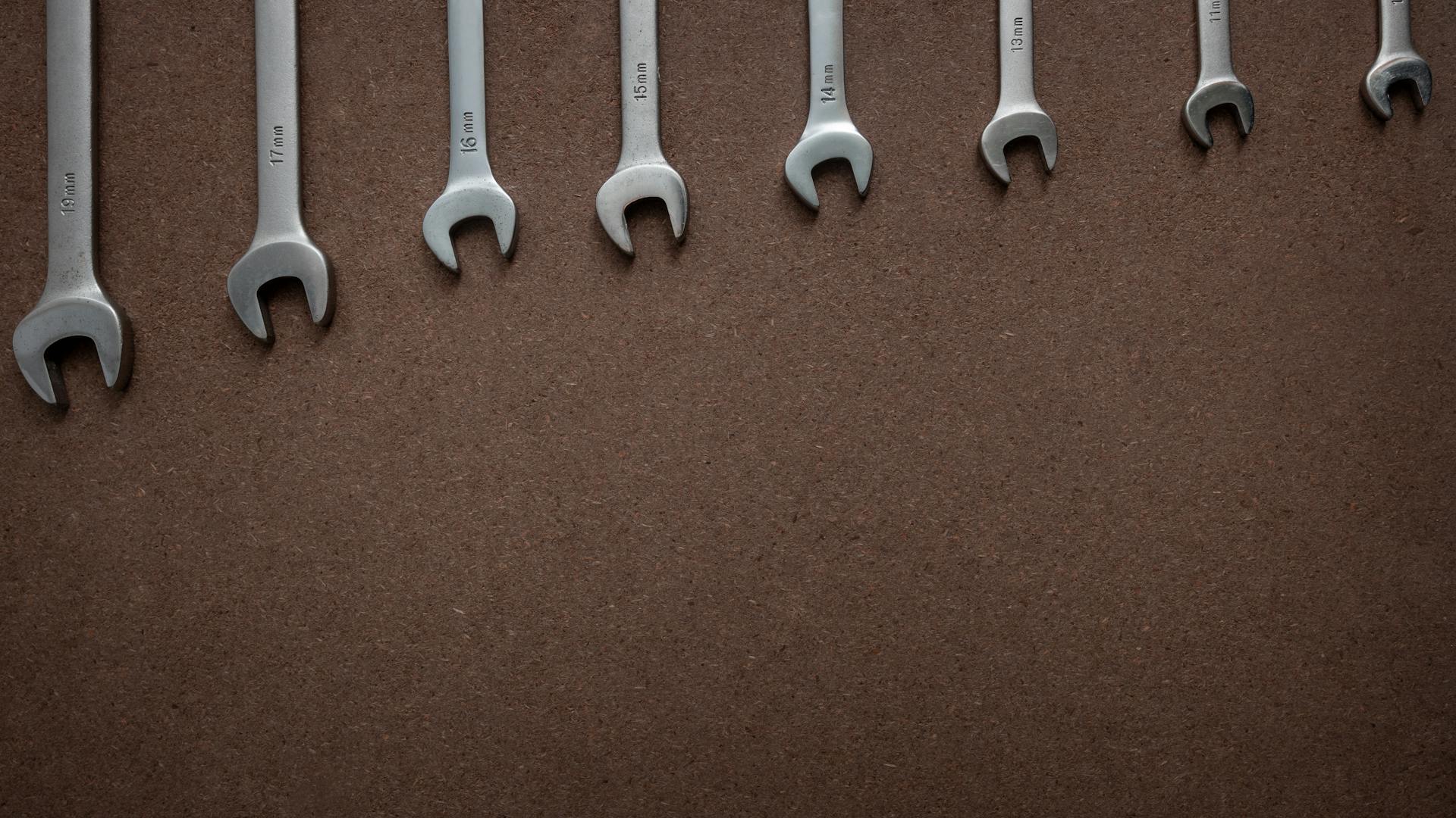 Spanners with different sizes on a wooden board. Top down view flat lay with workshop tools on a brown OSB board. Wooden background with wrenches lined up according to size and empty space...