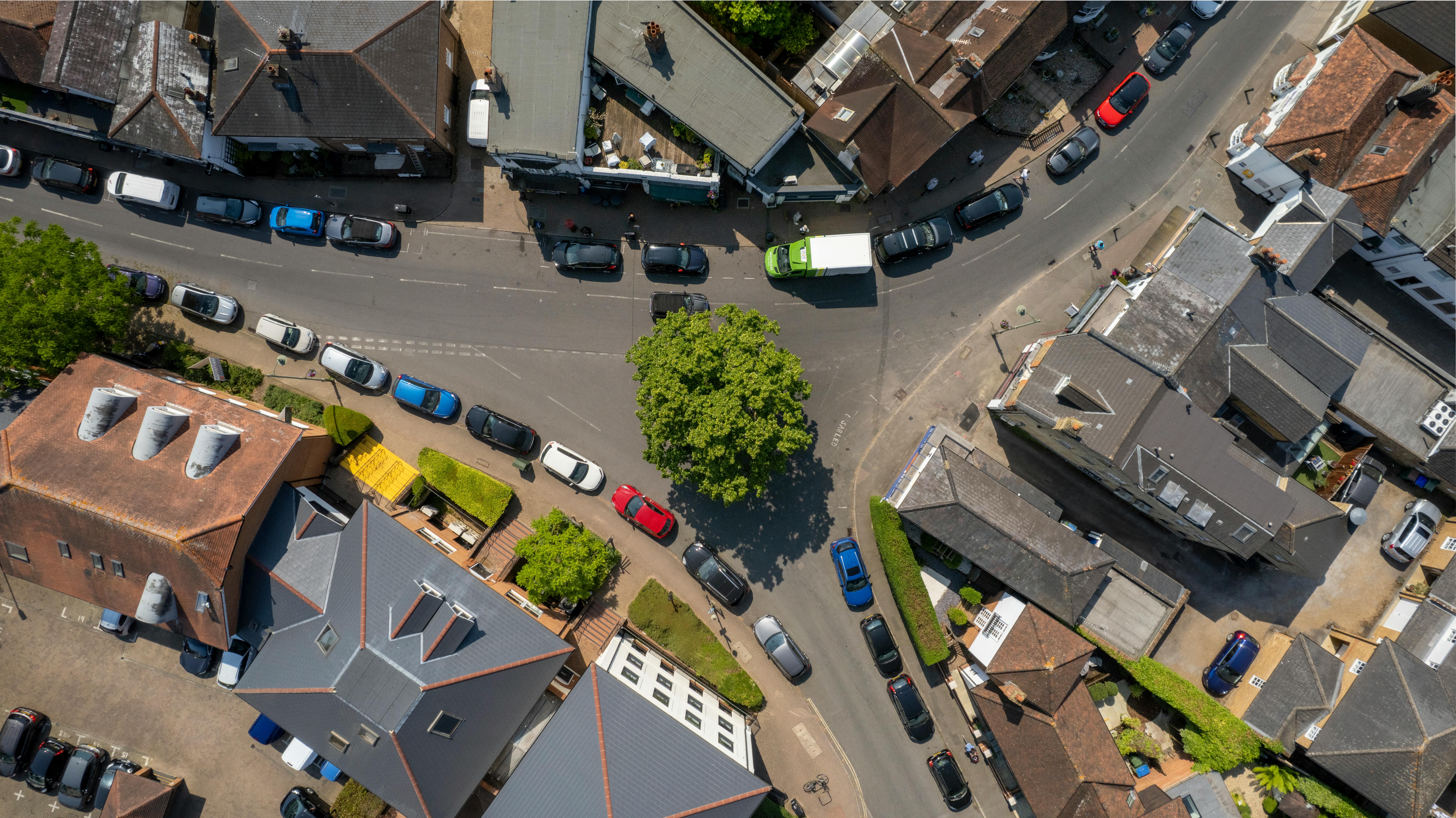 Overhead aerial view of a road intersection in Thames Ditton, England, with cars and rooftops in summer.