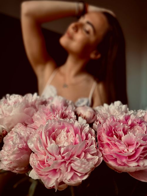 Free Delicate pink peonies in focus with a blurred woman in the background. Stock Photo