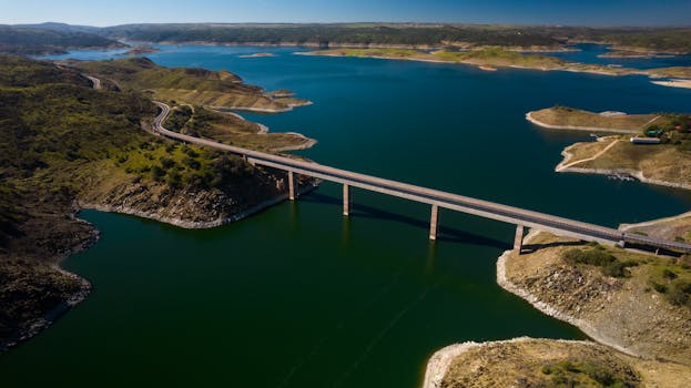 An aerial view captures a serene landscape with a bridge spanning over a calm reservoir in Cáceres, Spain.