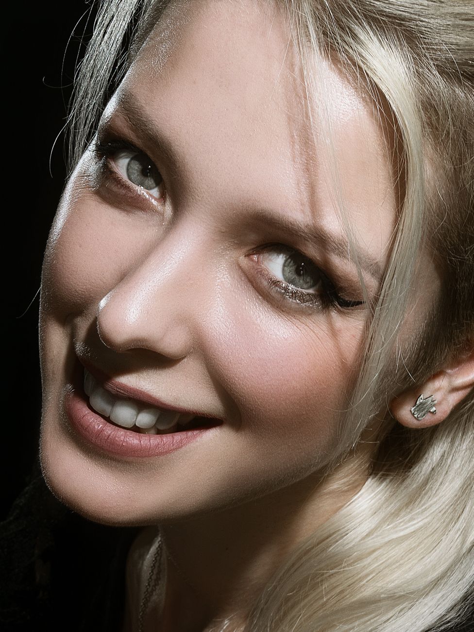 A close-up portrait of a smiling blonde woman with striking eyes and long hair.