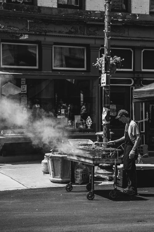 A man is cooking food on a grill in front of a building