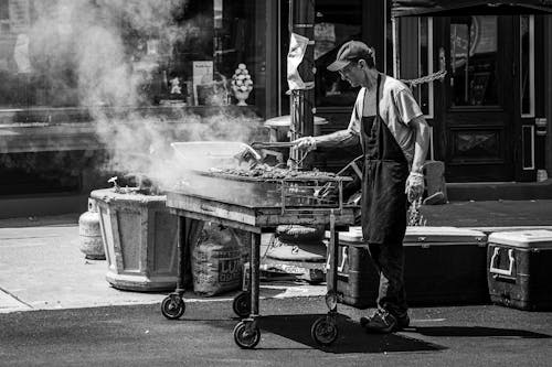 A man is cooking food on a grill in front of a building
