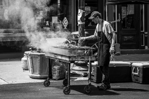 Free A grill master tends to a smoky barbecue on a city street, creating a vibrant urban scene. Stock Photo
