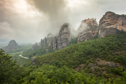 Captivating view of the Meteora rock formations in Greece enveloped in mist, surrounded by lush greenery.