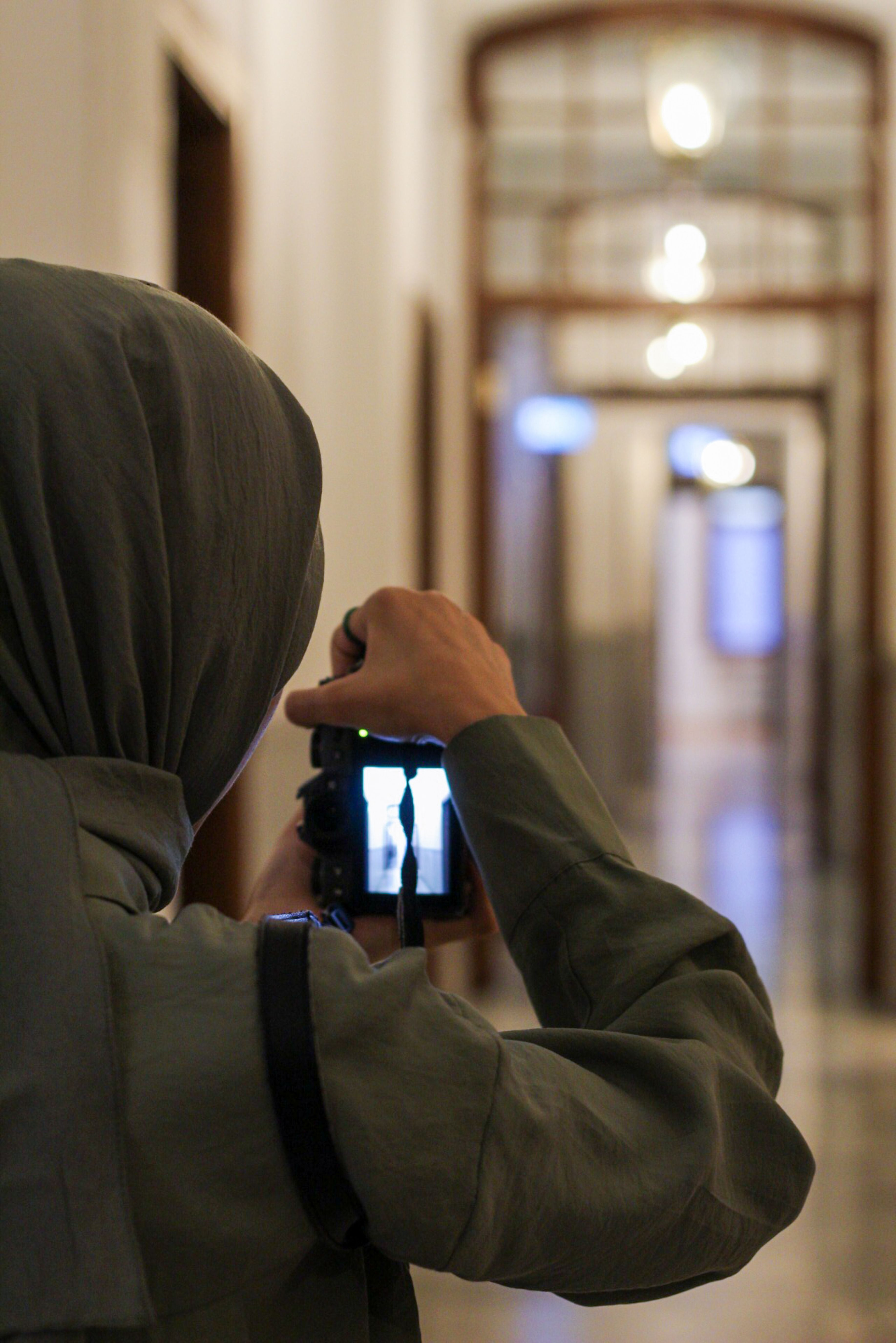 Person in a hoodie takes a photo inside a corridor, focusing on architectural details.