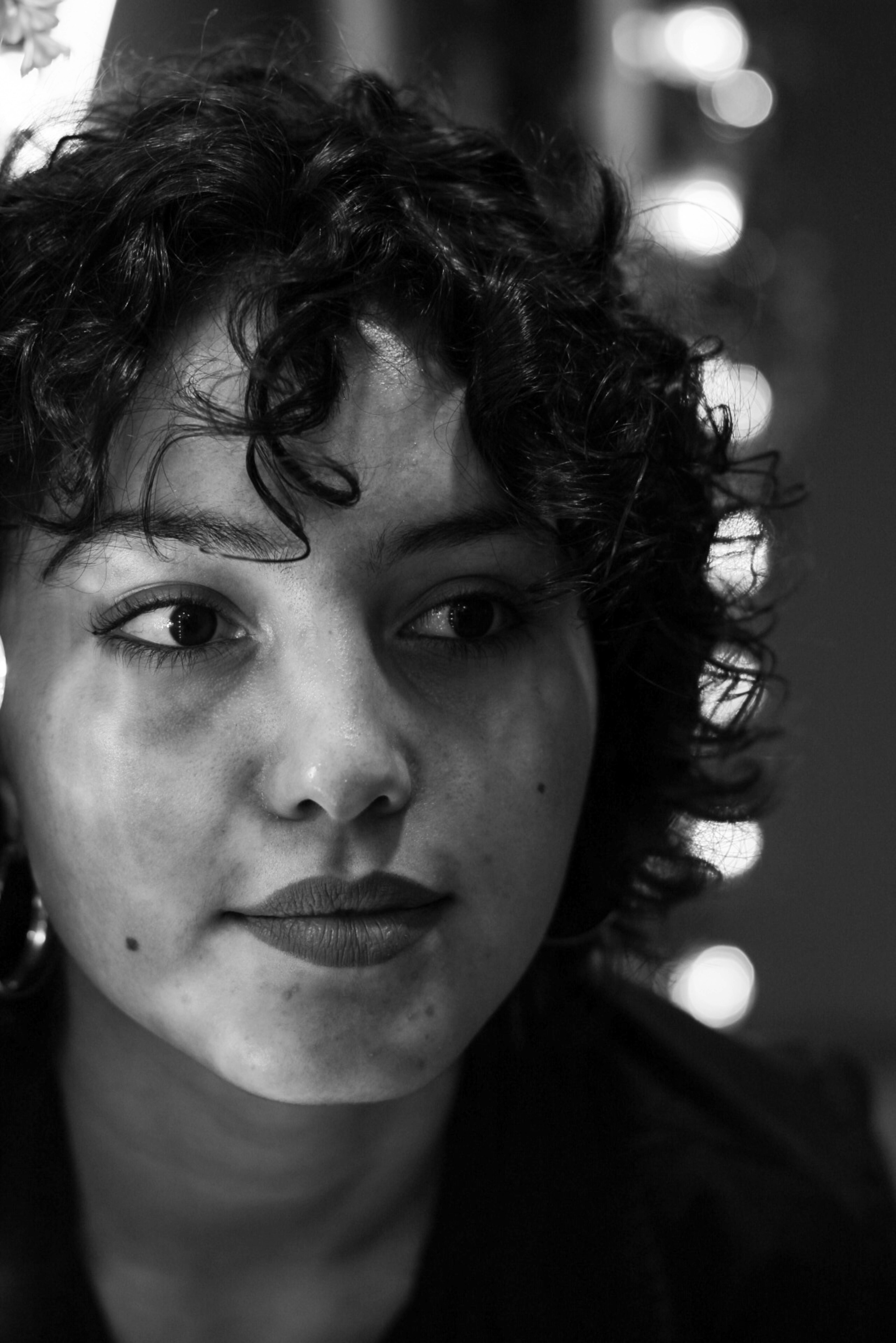 Close-up black and white portrait of a woman with curly hair and thoughtful expression.
