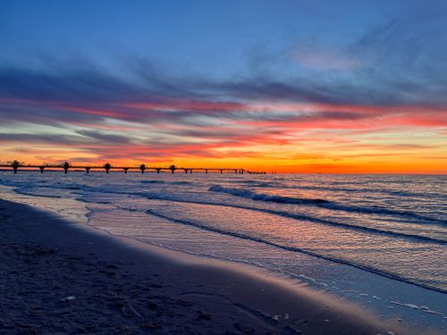 Free Vibrant sunset with dramatic skies over a pier and waves on a sandy beach. Stock Photo