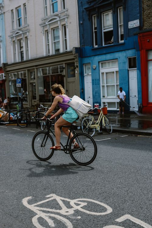 Free A cyclist rides through colorful streets of London featuring vibrant buildings and urban life. Stock Photo
