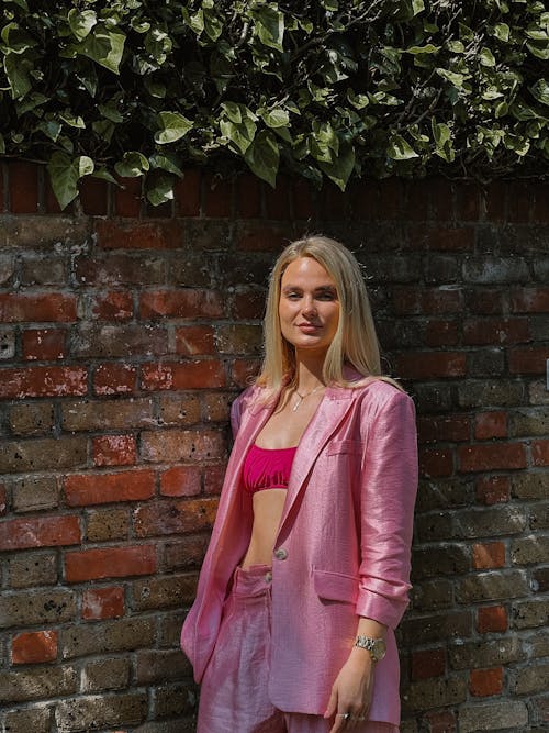 A Woman in a Pink Silk Suit Posing Against a Brick Wall