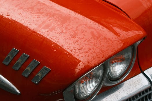 A vivid vintage red car hood and headlights with raindrops reflecting nostalgia and classic automotive design.