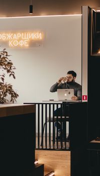 A man enjoys coffee while working on a laptop in a modern café setting.