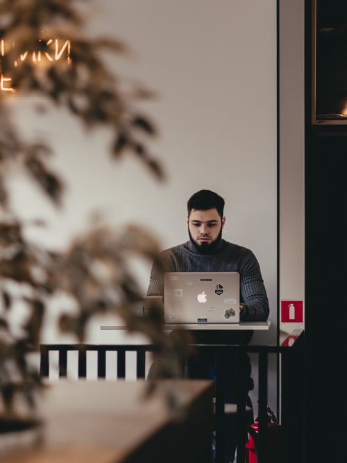 Free Man using laptop in a modern cafe, focused amidst a warm ambiance. Stock Photo