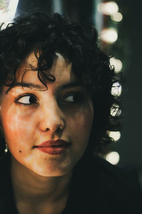 Free Intriguing close-up portrait of a woman with curly hair under ambient lighting. Stock Photo