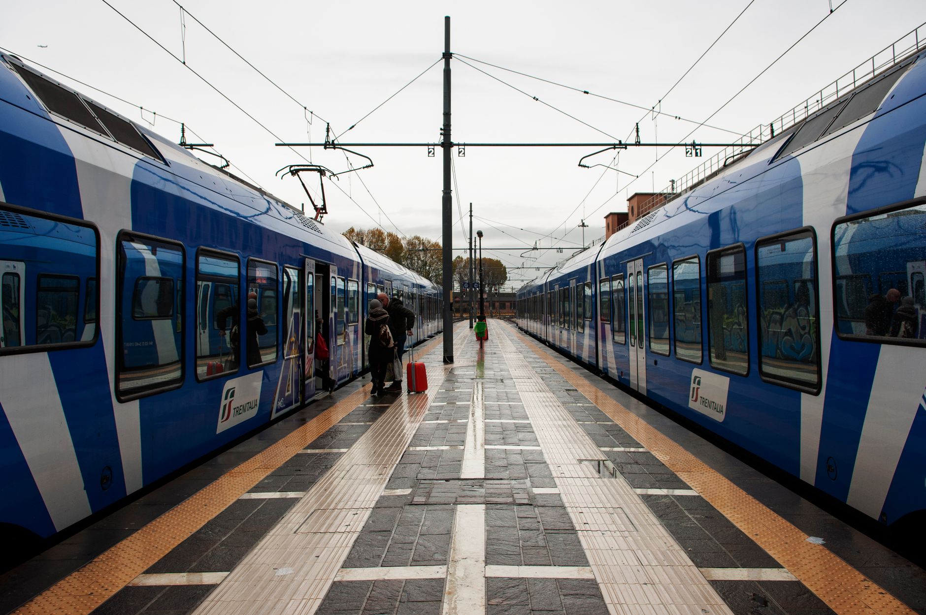 Trenitalia trains at an Italian station platform, symmetrical view of passengers boarding