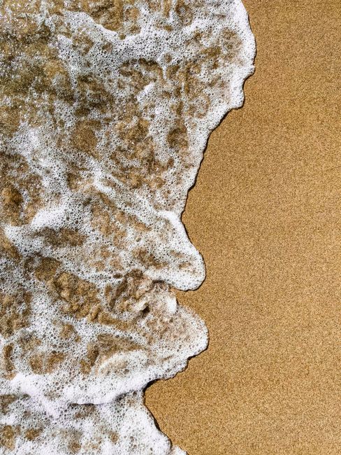 Foamy ocean waves gently washing over the sandy beach shore in summer.