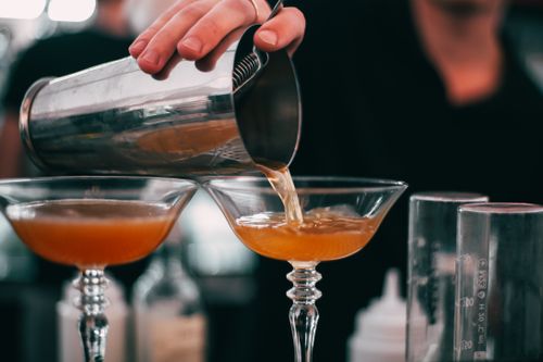 Free A bartender skillfully pouring cocktails into glasses with a cocktail shaker in a bar setting. Stock Photo