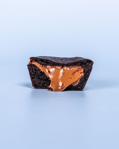 Free Close-up of a rich brownie with gooey caramel filling against a blue background. Stock Photo