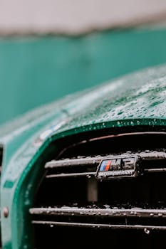 Detailed close-up of a car's front grill wet from rain, featuring water droplets and a sleek green color.