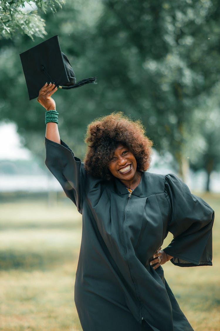 Smiling Graduate Holding Academic Hat In Raised Arm