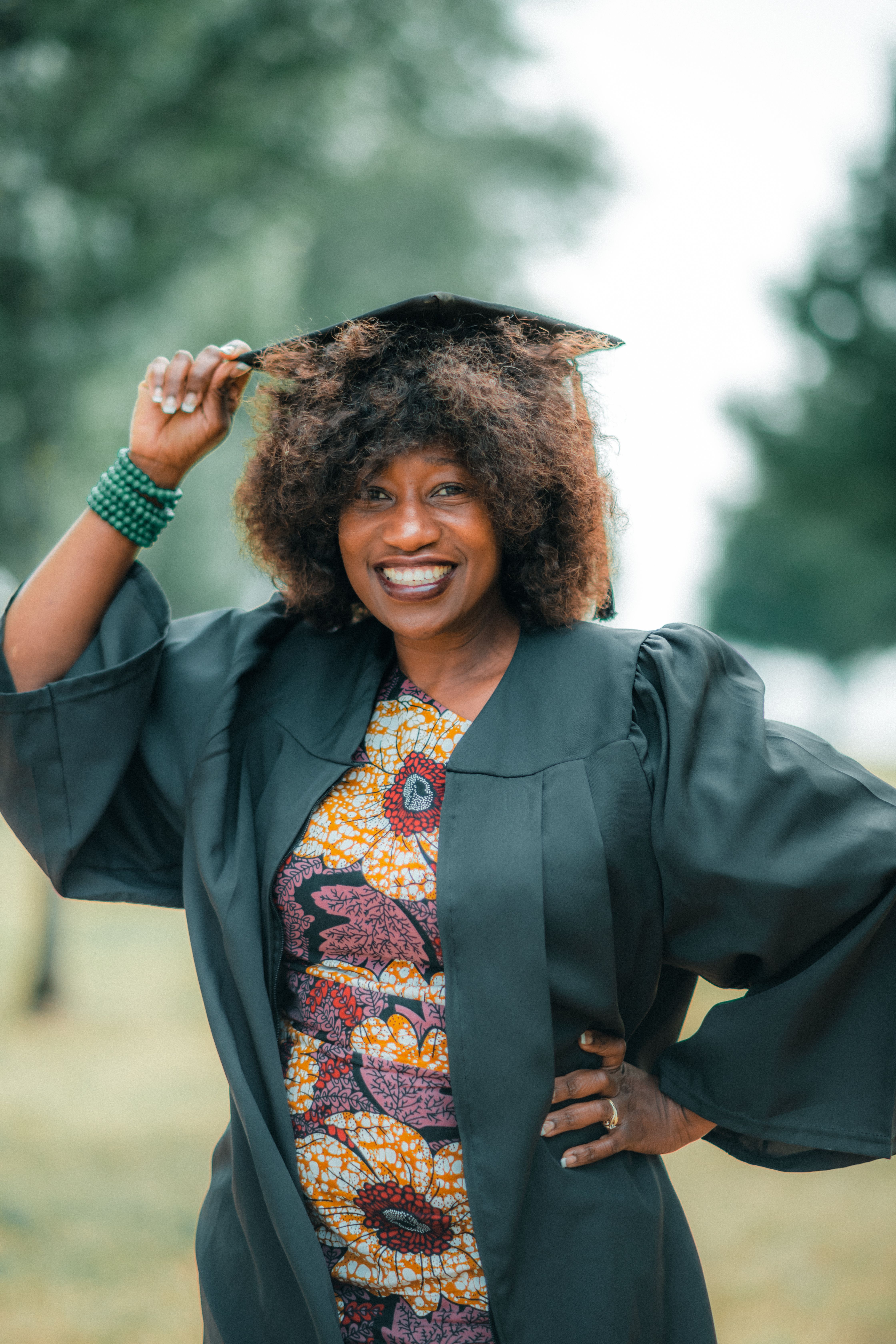 A happy graduate in a cap and gown smiles outdoors, celebrating achievement.