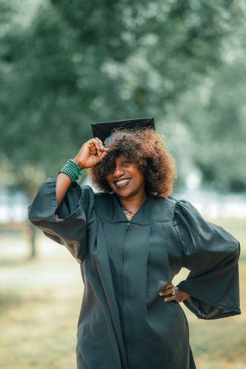 Photo of a Smiling Woman Wearing a Graduation Gown and Mortarboard Posing in a Park