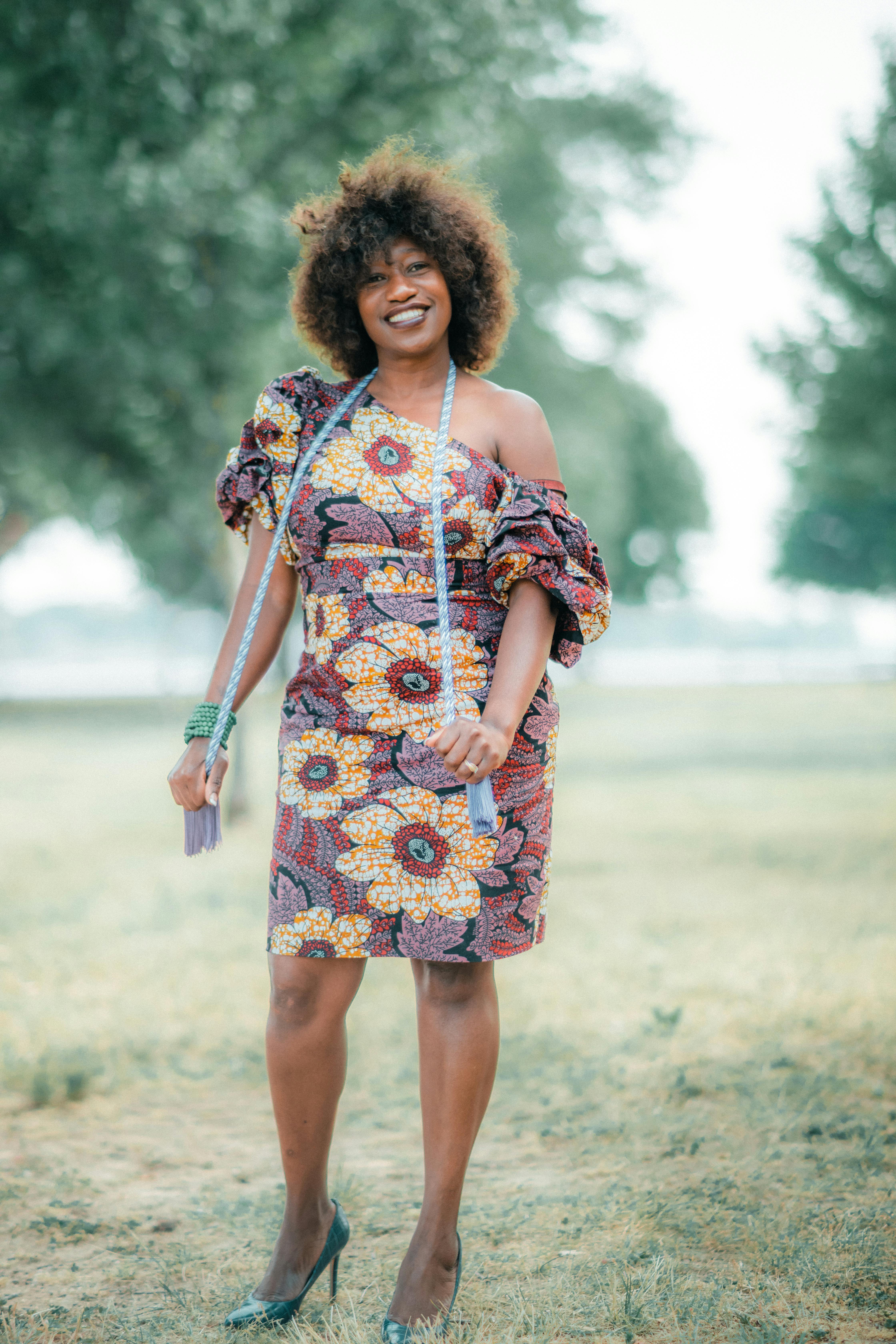 Free African woman smiling in a stylish floral dress and high heels outdoors. Stock Photo
