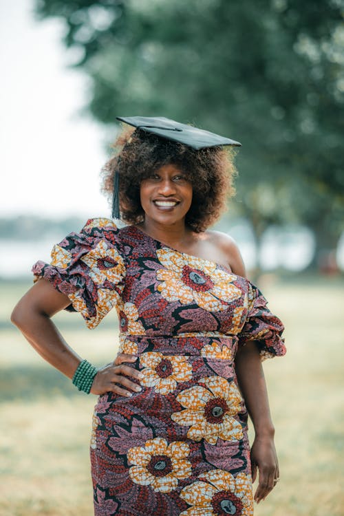 Woman Wearing a Floral Pattern Dress and Mortarboard Posing in a Park