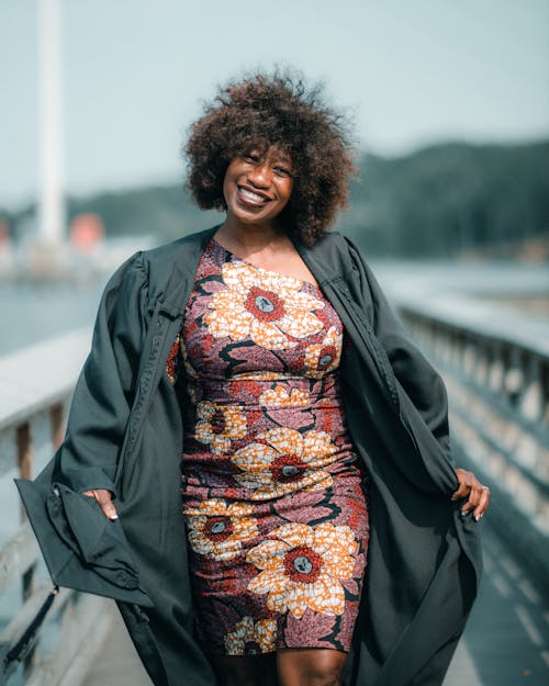 Woman Wearing a Graduation Gown and Floral Dress Posing on a Footbridge