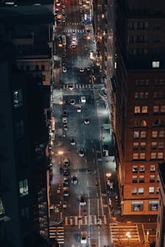 Aerial night shot of a busy urban street illuminated by bright city lights.