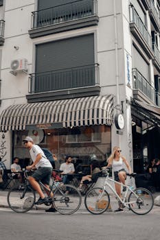 Man and woman cycling in a lively urban area with a café background.