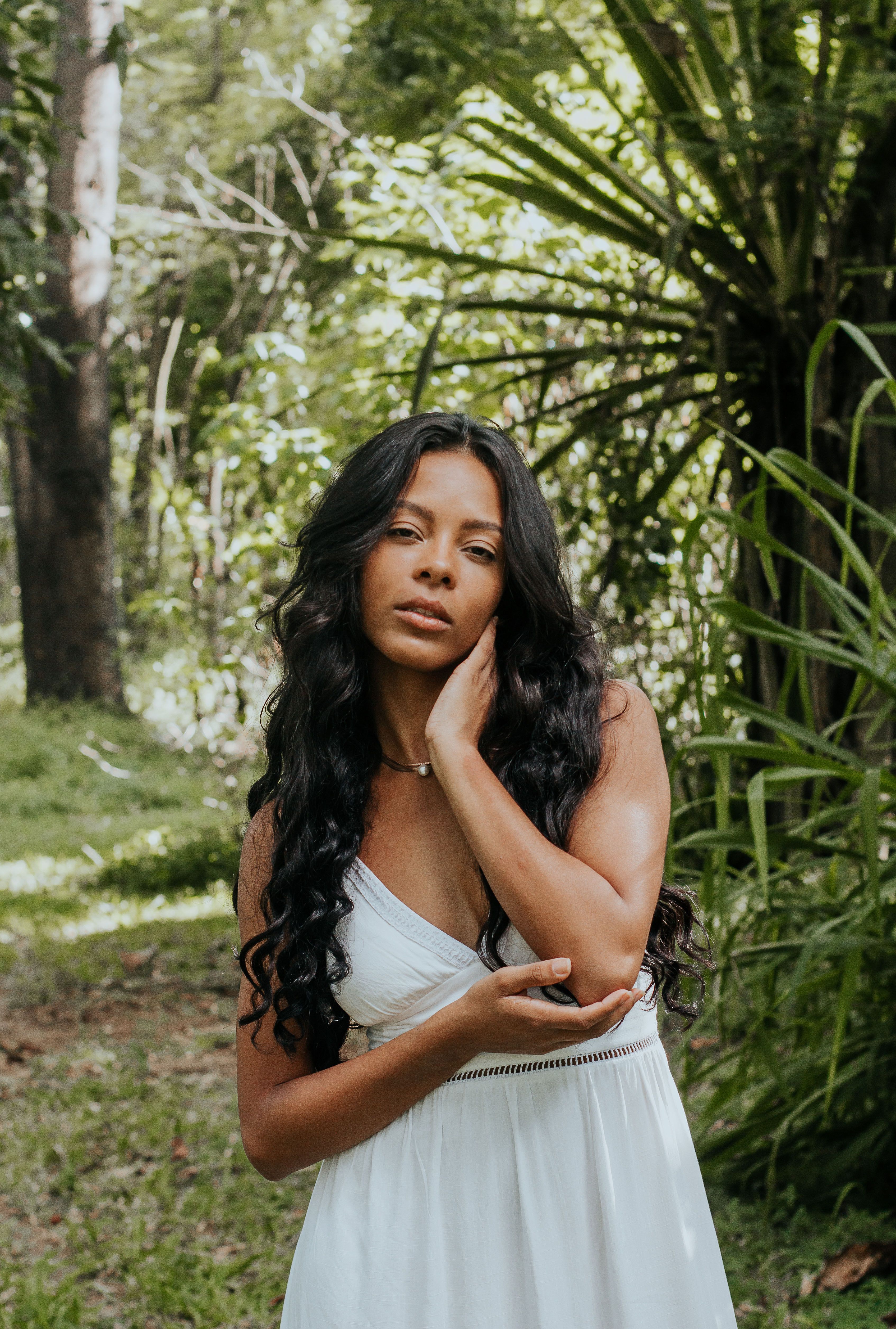 Elegant woman in a white dress posing gracefully in a lush, green forest setting.