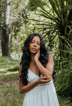 Elegant woman in a white dress posing gracefully in a lush, green forest setting.