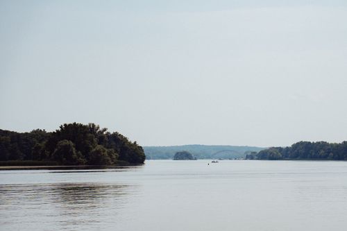 Free A tranquil lake scene with lush forested shores under a clear sky. Stock Photo