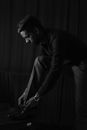 Grayscale Photo of Man in Dress Shirt and Pants Tying His Shoelaces