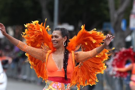 Brightly dressed woman in an orange costume with feathers dancing joyfully in a parade.