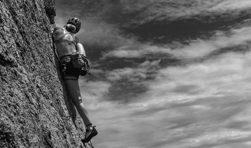 Free Bold black and white image of a woman rock climbing under a cloudy sky, showcasing adventure. Stock Photo