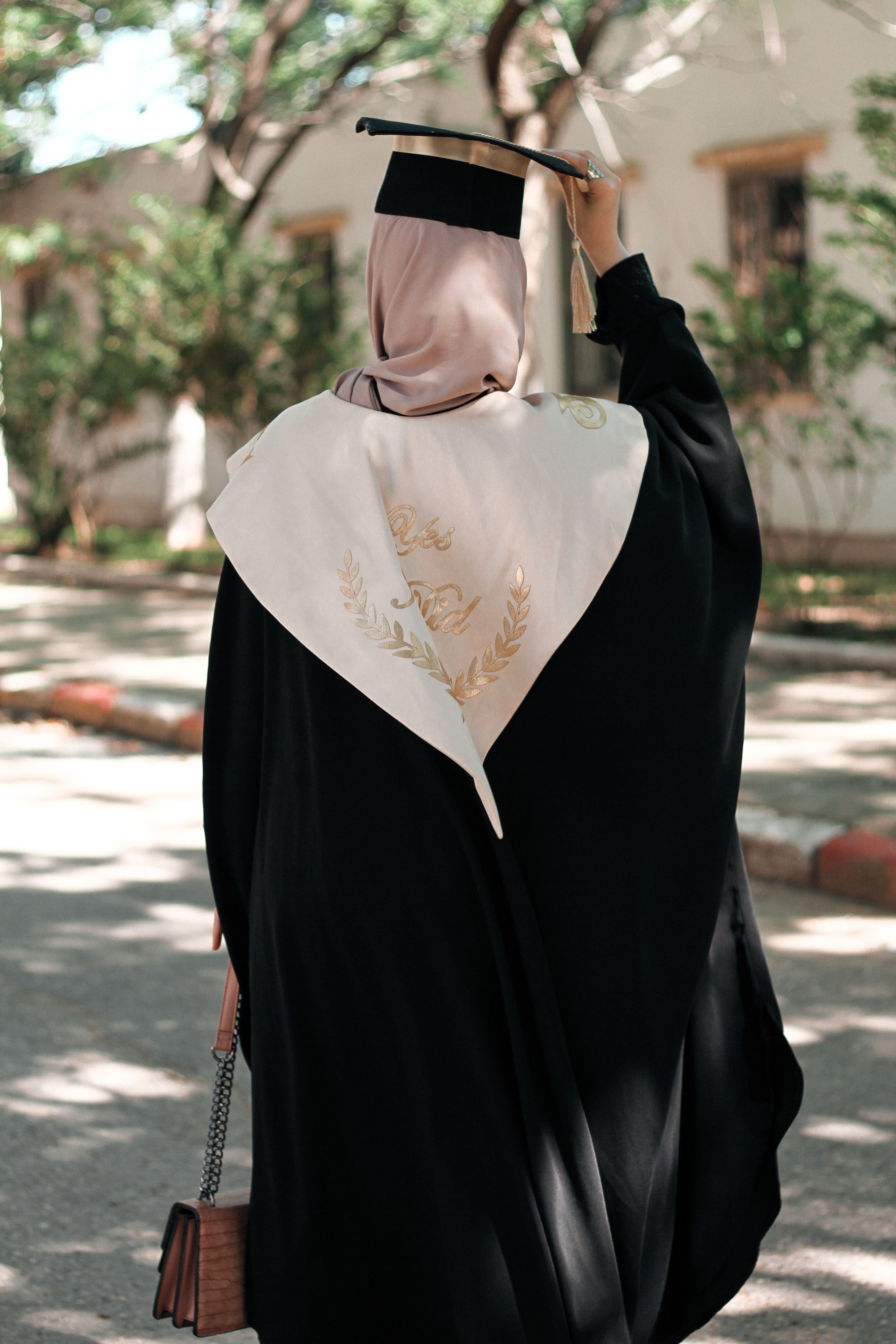 Uma mulher usando hijab e vestido de formatura comemora sua conquista ao ar livre em Argel.