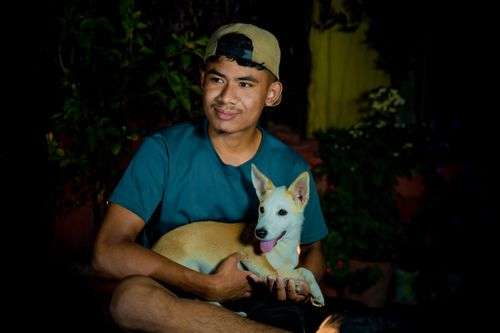 Free Portrait of a young man sitting outdoors with his dog, smiling at night. Stock Photo