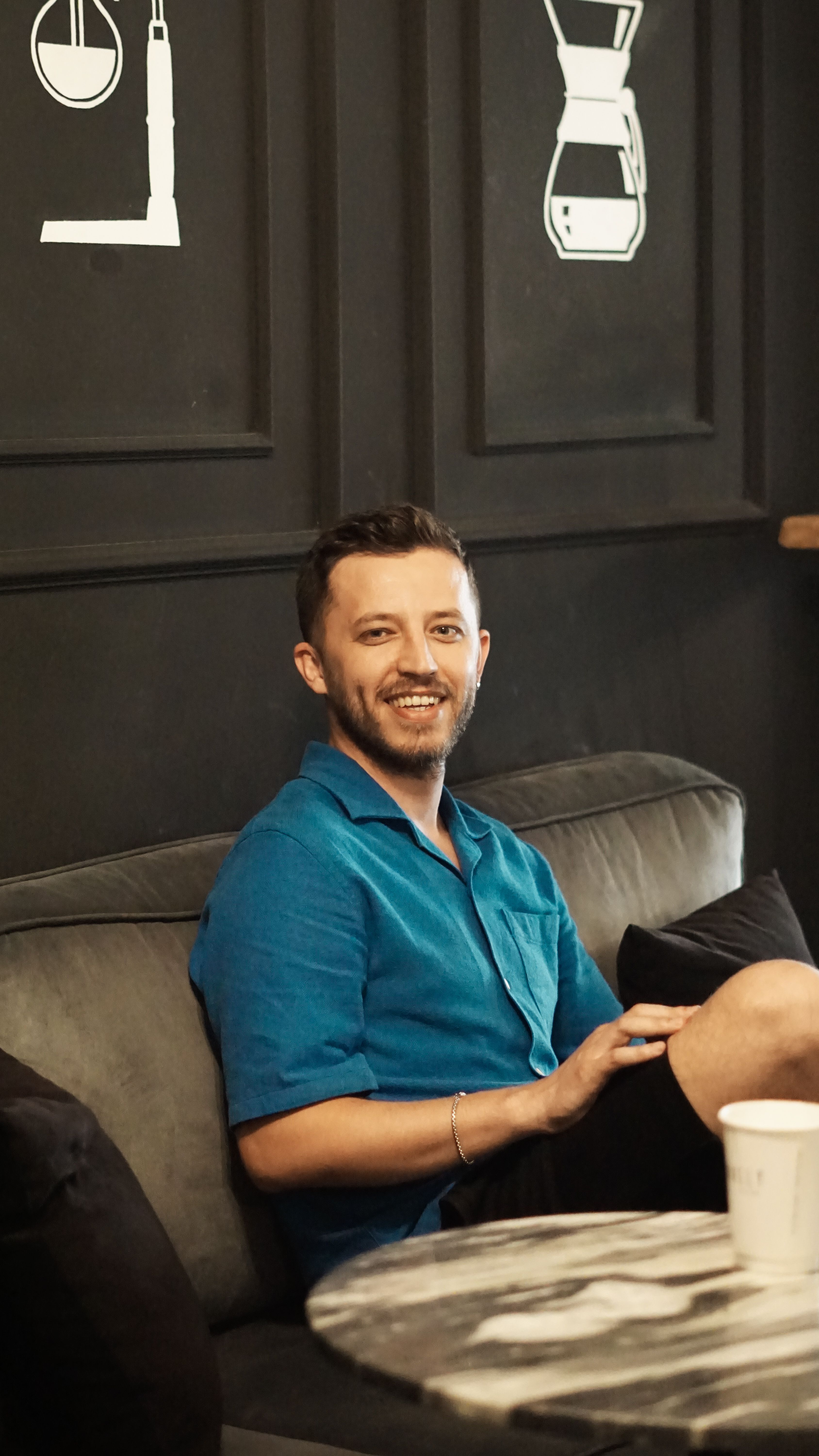 A young man in a blue shirt enjoying his coffee in a trendy indoor cafe setting.