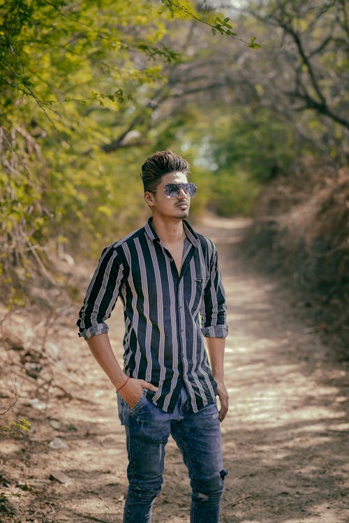 Young Man in a Striped Shirt and Jeans Standing on a Country Road 