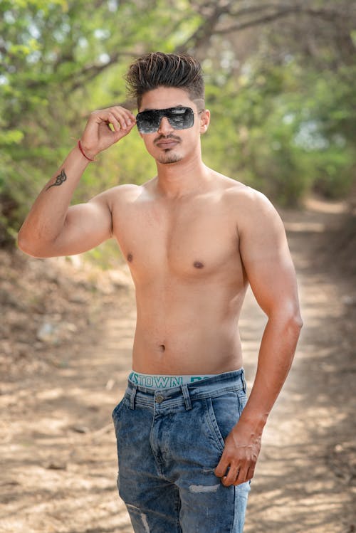 Young Shirtless Man Standing on the Country Road and Fixing his Eyeglasses 