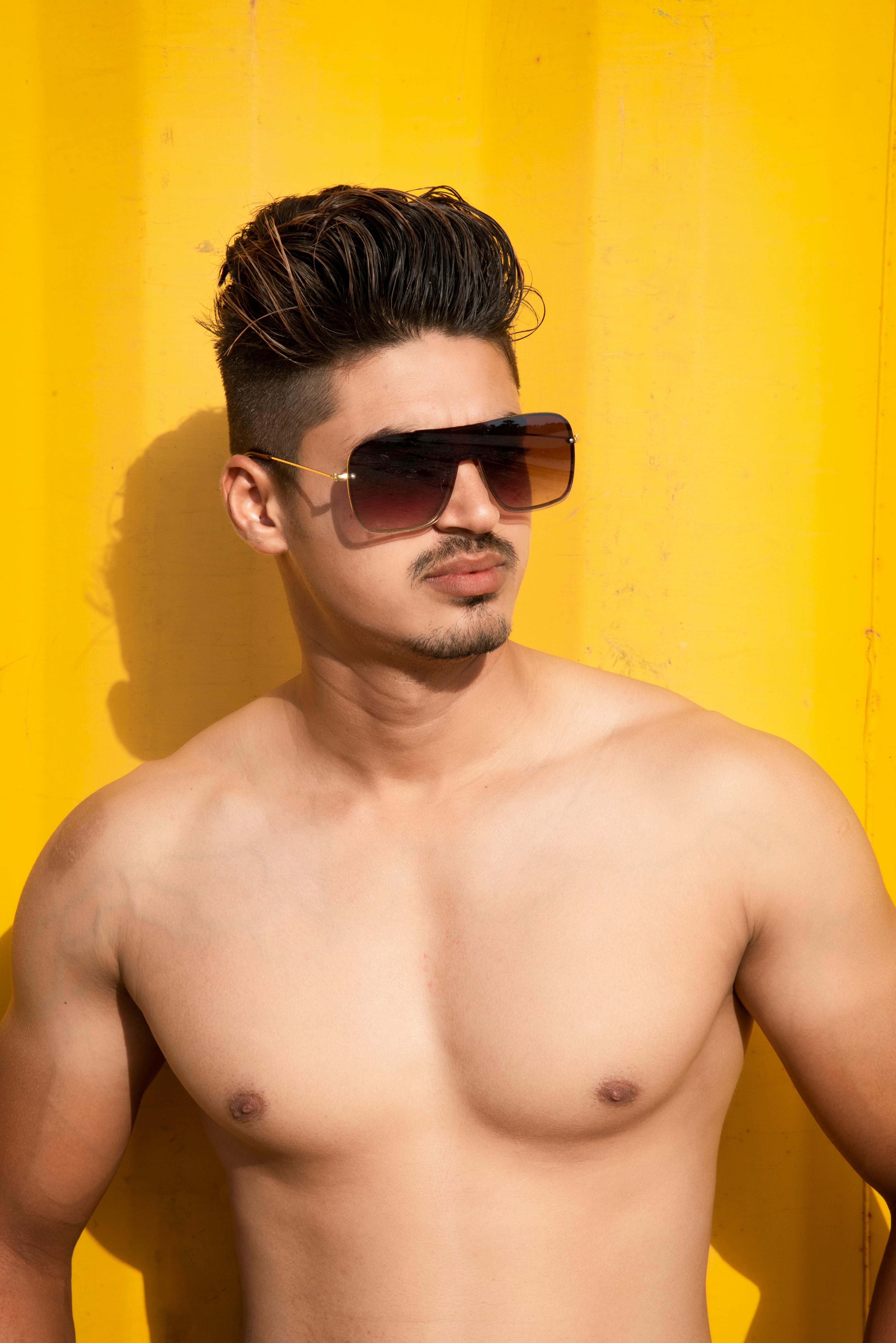 Confident young man posing with sunglasses on a bright yellow background in Mandvi, India.