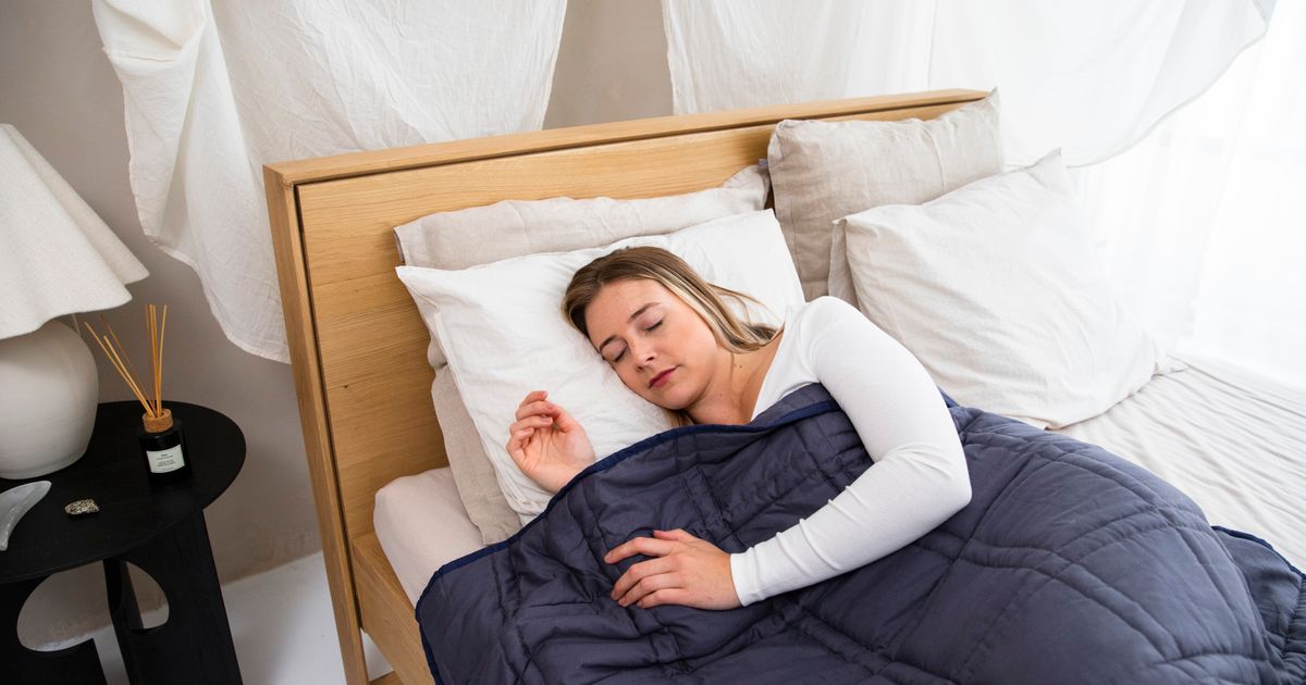 A woman asleep under a navy quilted weighted blanket