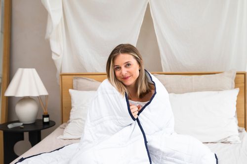 Free A woman wrapped in a blanket on a bed in a modern bedroom setting, enjoying a relaxed morning. Stock Photo
