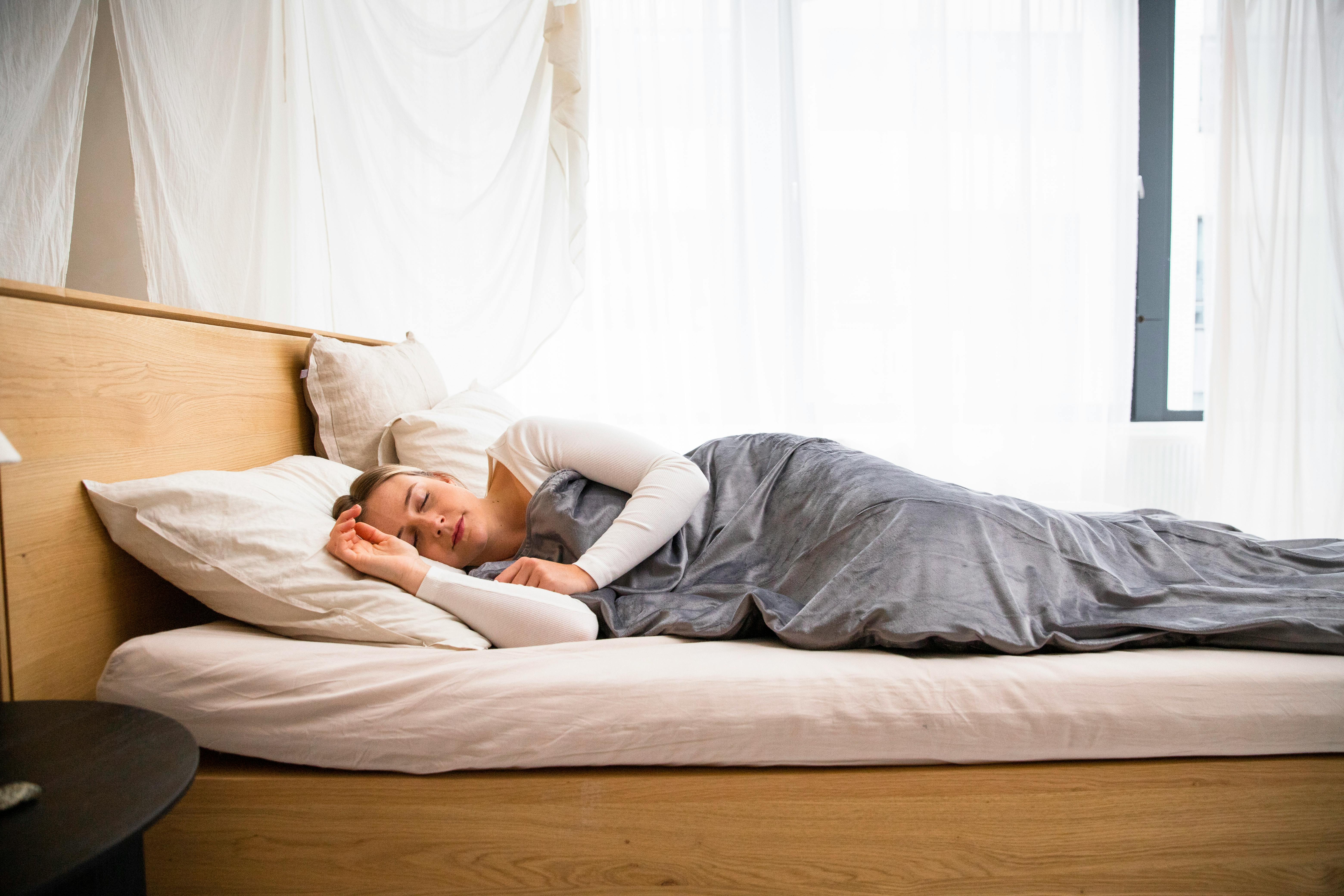 A woman peacefully sleeping in a well-lit modern bedroom with minimal decor.