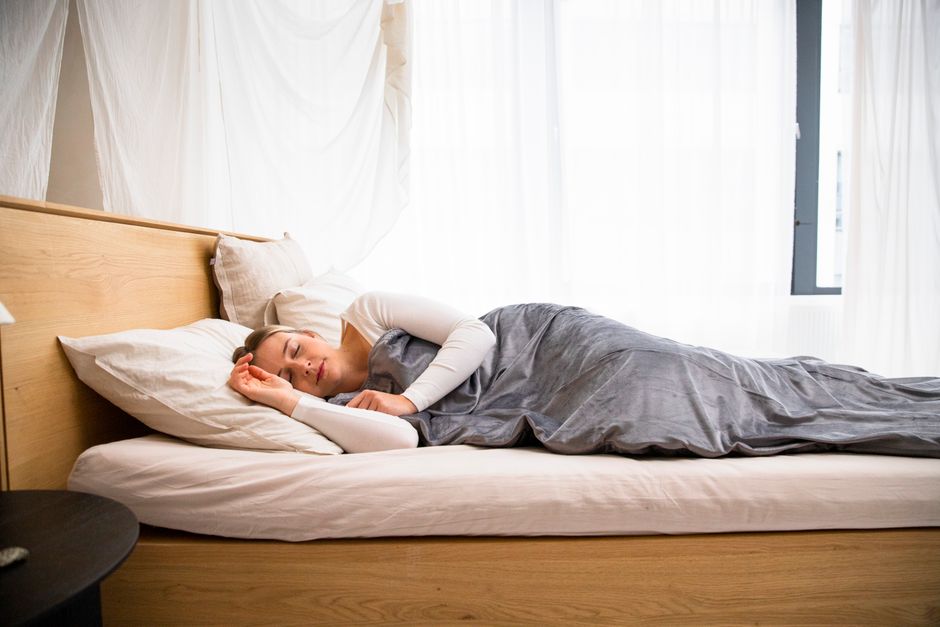 How Weighted Blankets Reduce Anxiety and Improve Sleep Quality A woman peacefully sleeping in a well-lit modern bedroom with minimal decor.