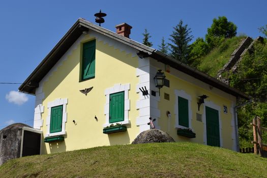 Picturesque yellow cottage with green shutters in Ghimeș-Făget, Romania, surrounded by lush greenery.